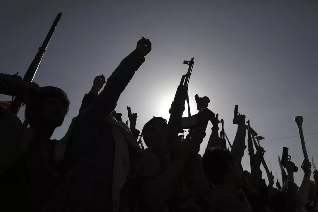 Siluete grupe ljudi koji drže različito oružje u zraku ispred jakog sunca.