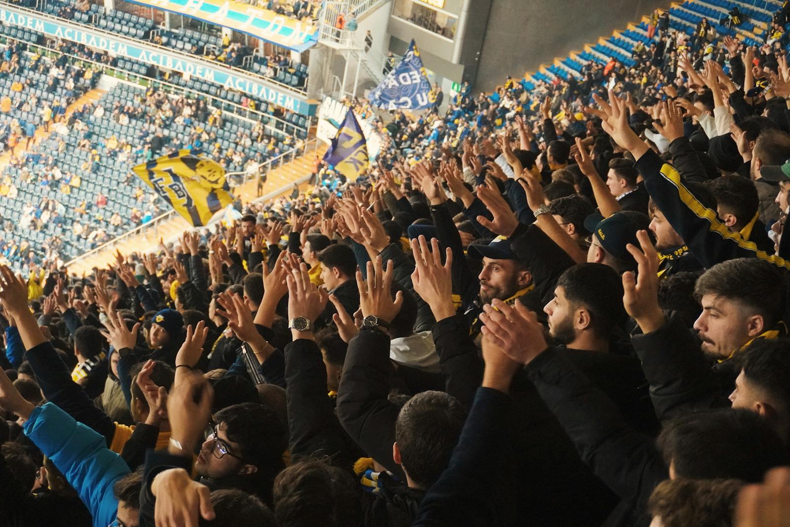 Energetic fans with raised hands in a stadium, supporting their soccer team with enthusiasm.