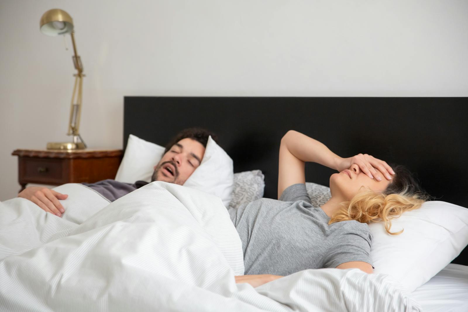 A couple in bed, with one partner covering their face due to the other's snoring.