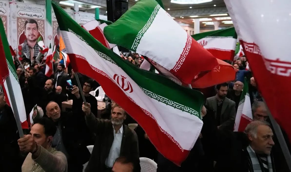 Grupa ljudi maše iranskim zastavama na skupu.