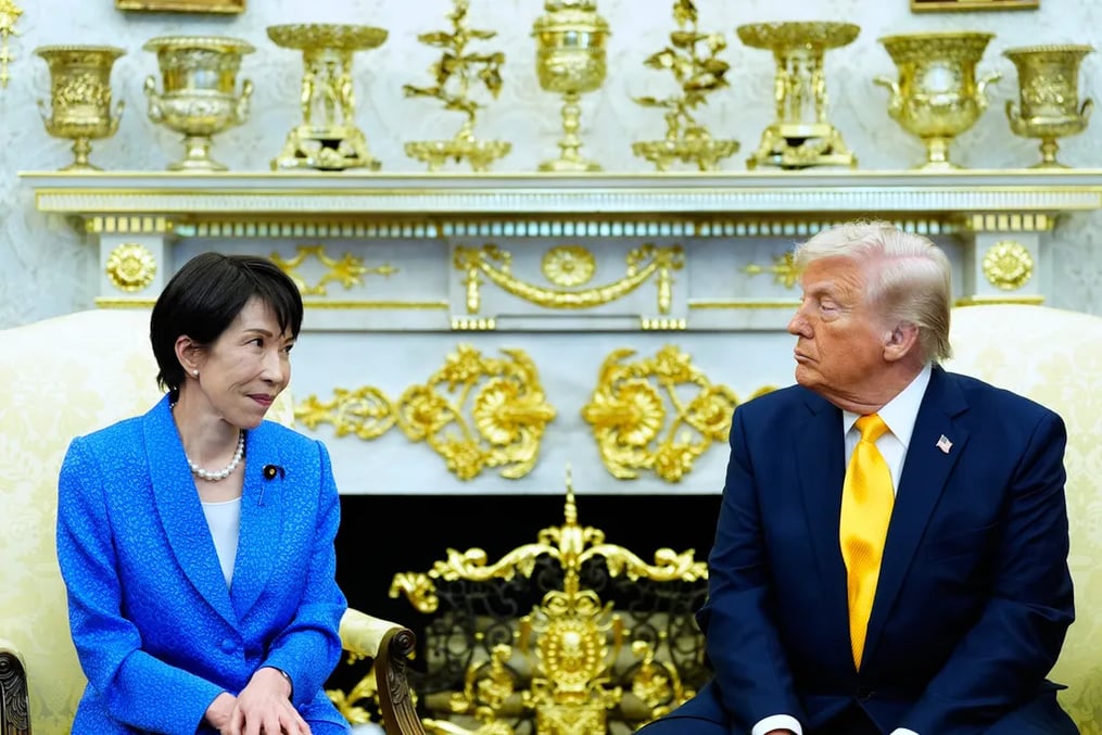 Donald Trump i žena u plavom odijelu sjede jedan pored drugog, ispred ukrašenog kamina.