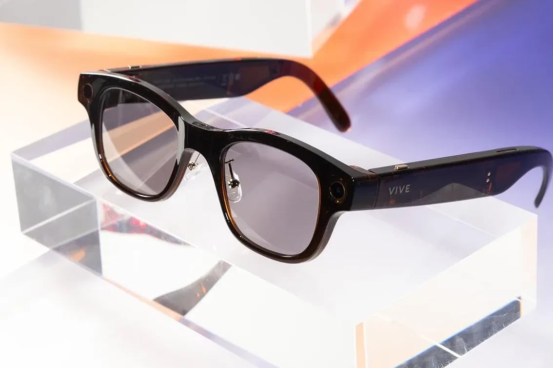 HTC Vive Flow naočare sa tamnim okvirima i zatamnjenim staklima, postavljene na prozirnu postolje