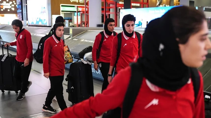 Iranske fudbalerke u crvenim dresovima i crnim hidžabima vuku prtljag na aerodromskoj pokretnoj traci.