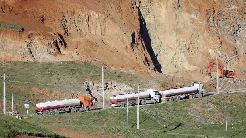 Tri kamiona cisterne sa prikolicama voze se uz put pored strmog pješčanog nasipa.