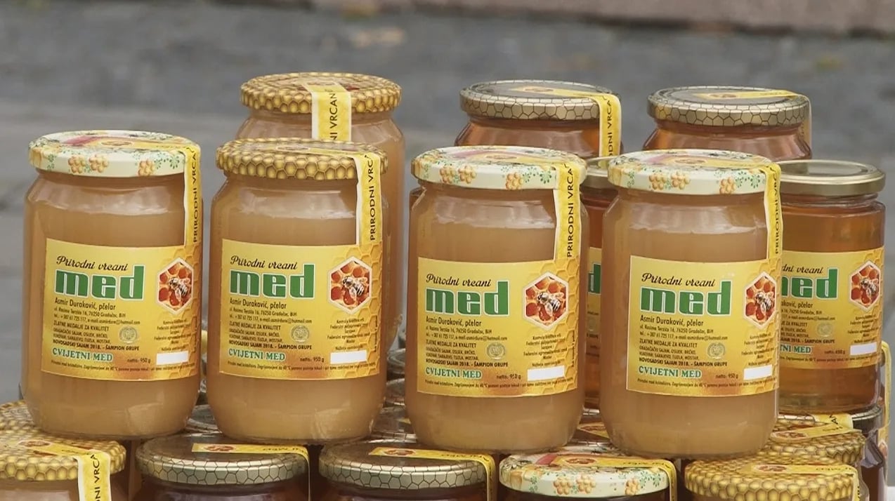 Više staklenih teglica punih meda, složenih jedne do drugih. Na svakoj teglici nalazi se žuta etiketa sa slikom pčele, saća i natpisima 'Prirodni vrcani med', te podacima o proizvođaču i nagradama.