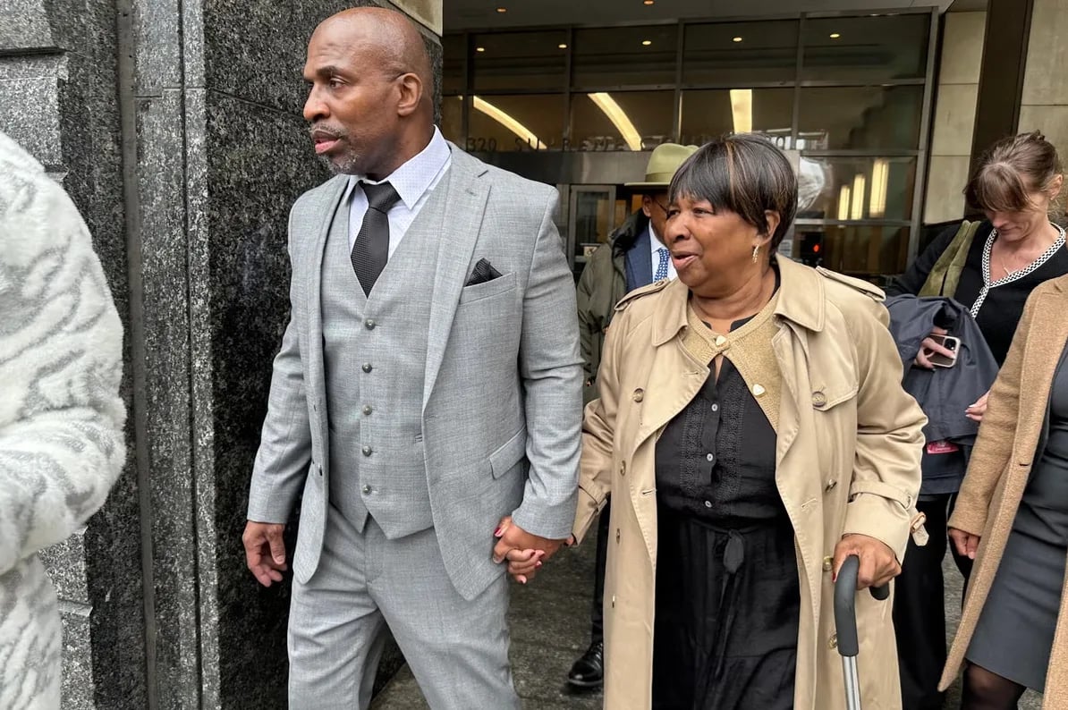 Muškarac u sivom odijelu i žena u bež baloneru drže se za ruke ispred zgrade.