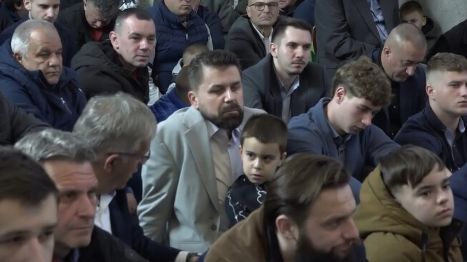 Grupa muškaraca i dječak sjede zajedno, fokus na djeci i odraslima.