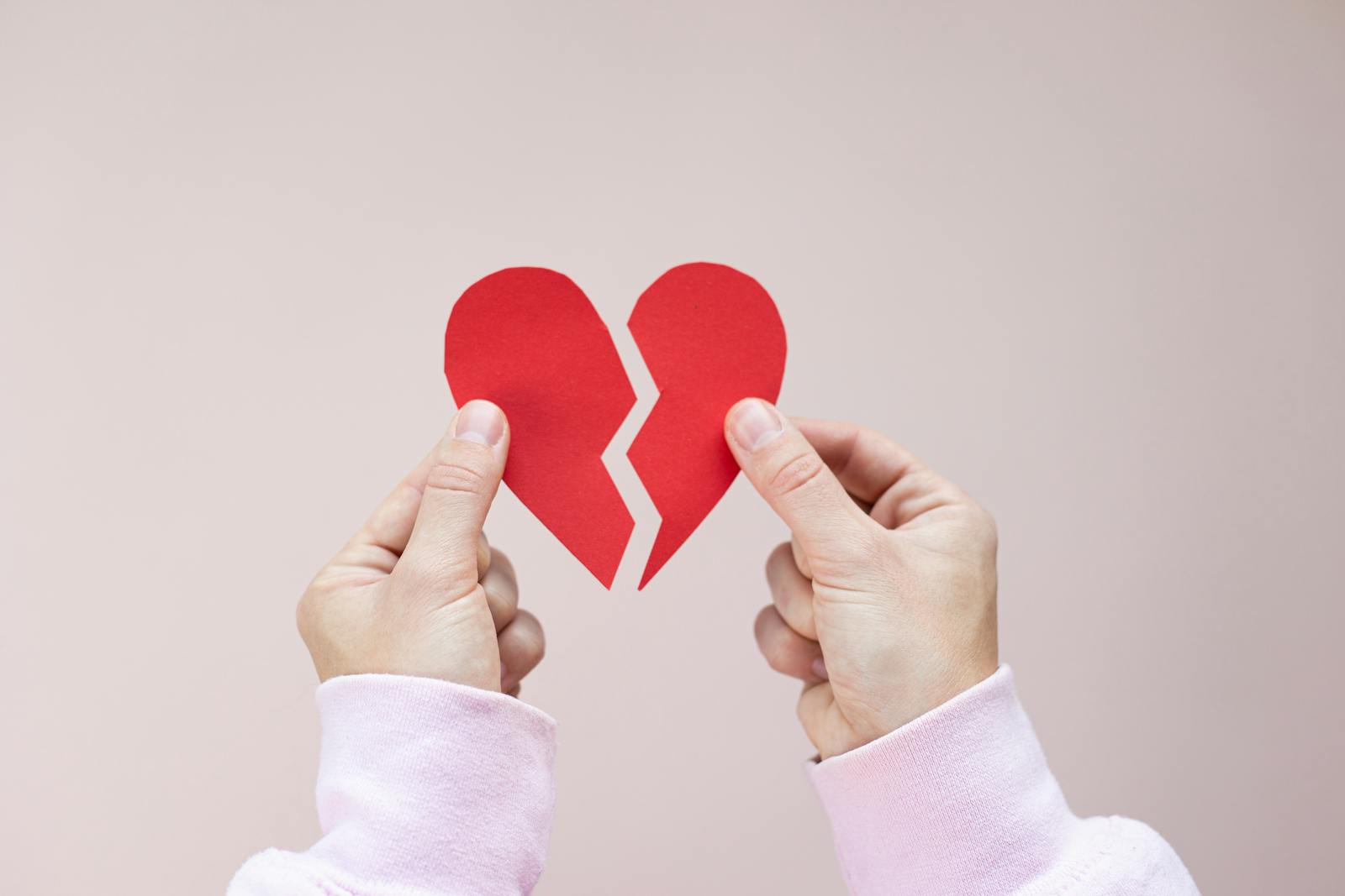 Close-up of hands holding a broken red paper heart symbolizing heartbreak and love.