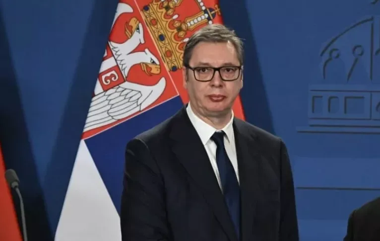 Aleksandar Vučić, predsjednik Srbije, stoji ispred zastave.