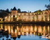 Osvijetljena tvrđava u Jajcu noću, reflektovana u vodi rijeke.