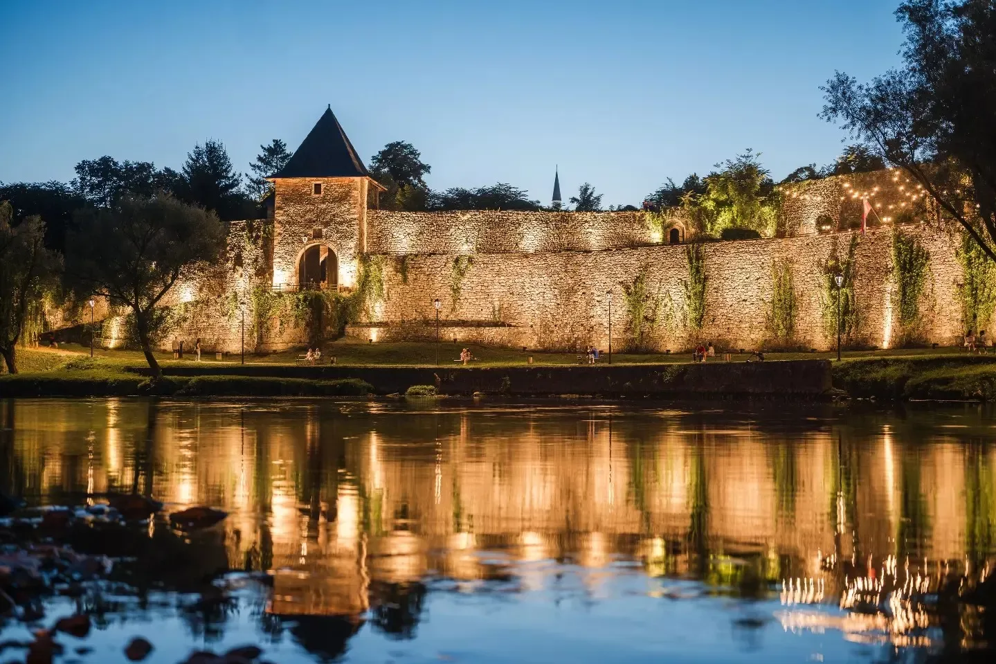 Osvijetljena tvrđava u Jajcu noću, reflektovana u vodi rijeke.