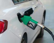 Close-up of a green nozzle refueling a white car at a gas station.