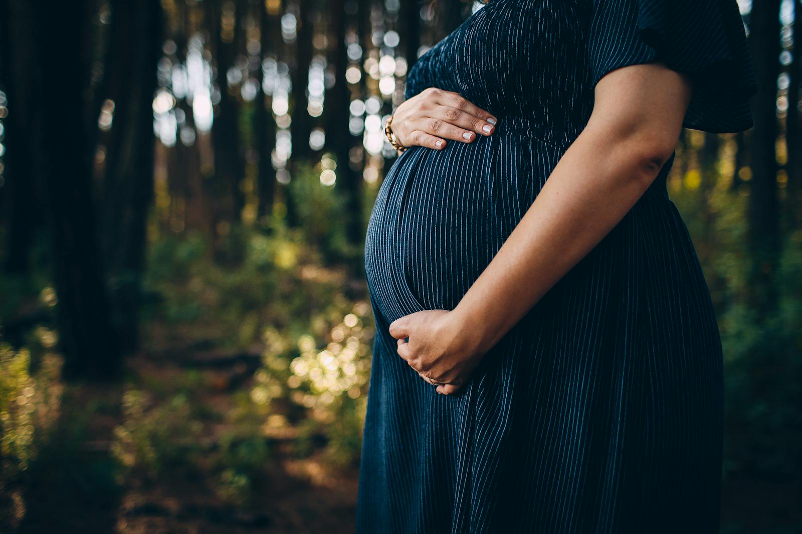 A peaceful moment of a pregnant woman embracing nature in a sunlit forest.