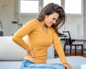 Žena osjeća bol u leđima, drži se za leđa.