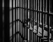 Crno-bijela fotografija rešetaka zatvorske ćelije.