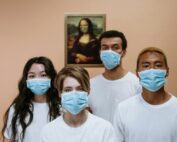 A diverse group wearing masks stands in front of a masked Mona Lisa painting.