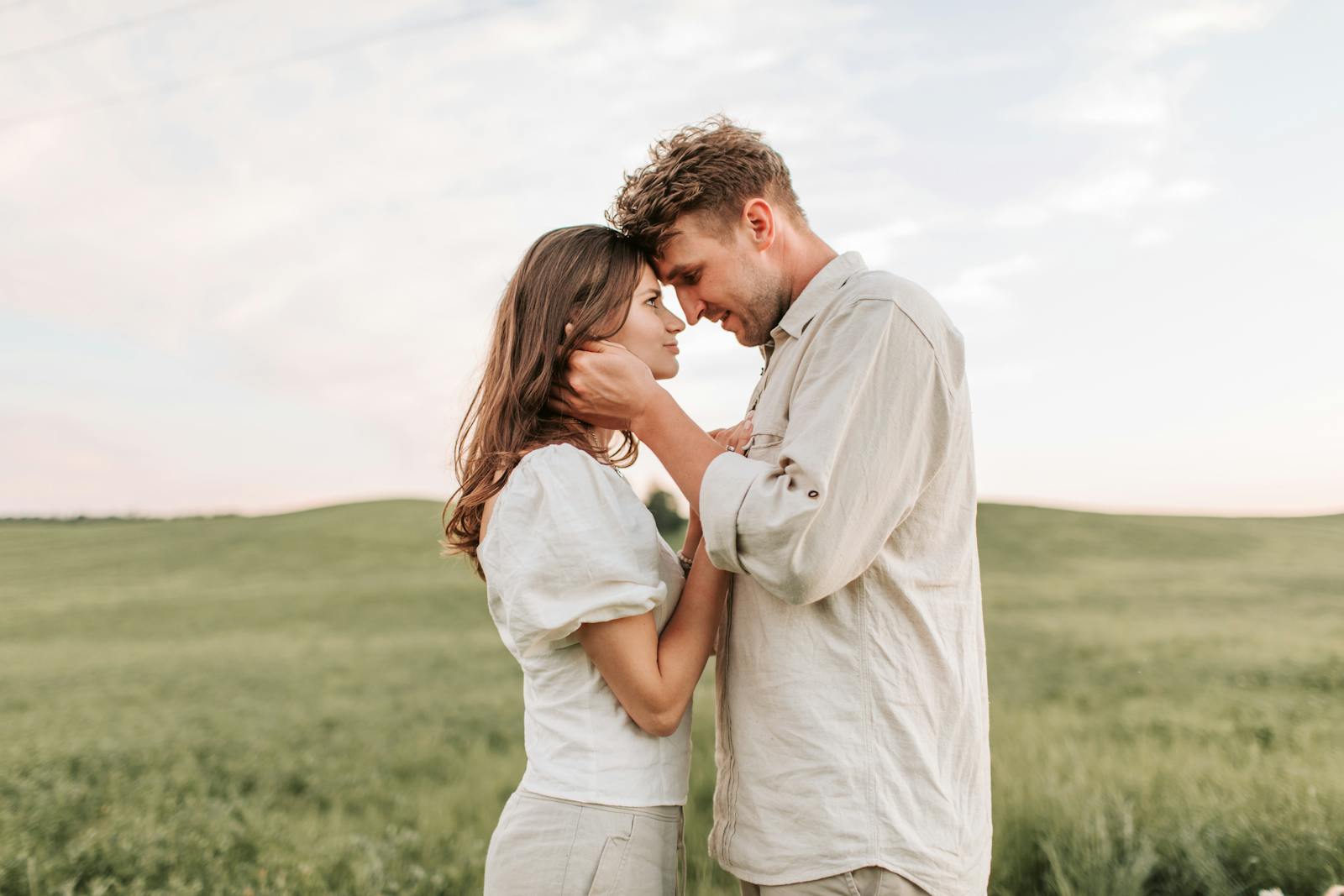 A loving couple embraces in a picturesque field during sunset, capturing a romantic moment.