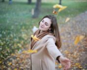 Young woman with arms outstretched, delighting in fallen leaves in a Paris park during autumn daytime.