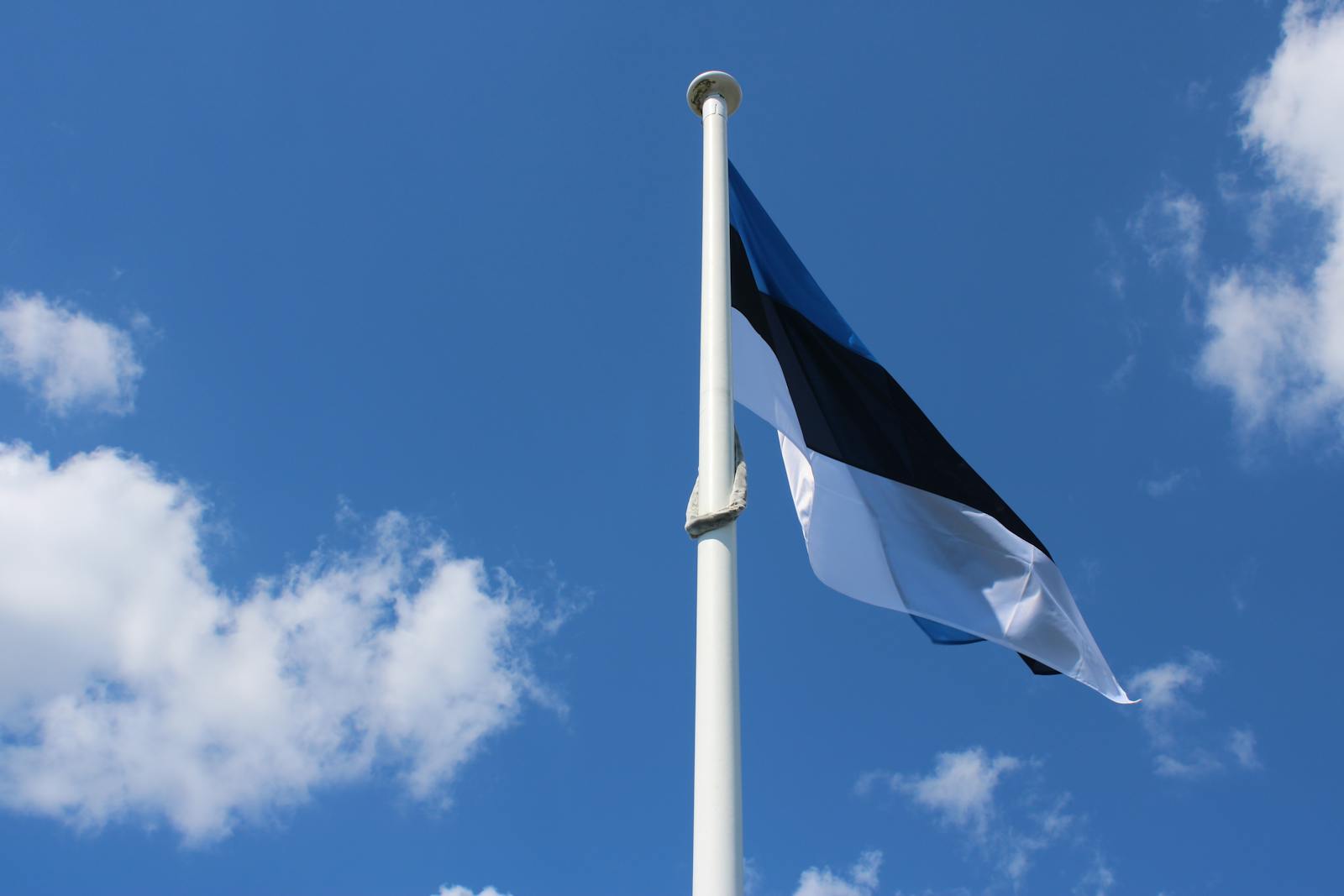 High view of Estonian flag fluttering against a vibrant blue sky with scattered clouds.