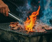 Close-up of grilling meat with vibrant flames and smoky aura, showcasing outdoor cooking.