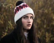 A thoughtful young woman wearing a knit hat in an outdoor winter setting.