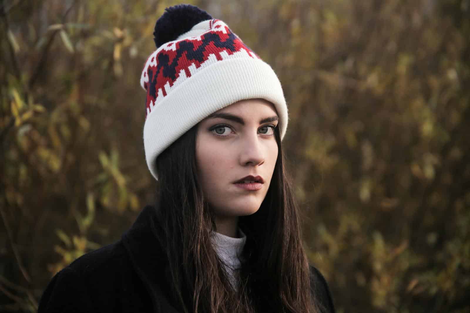 A thoughtful young woman wearing a knit hat in an outdoor winter setting.