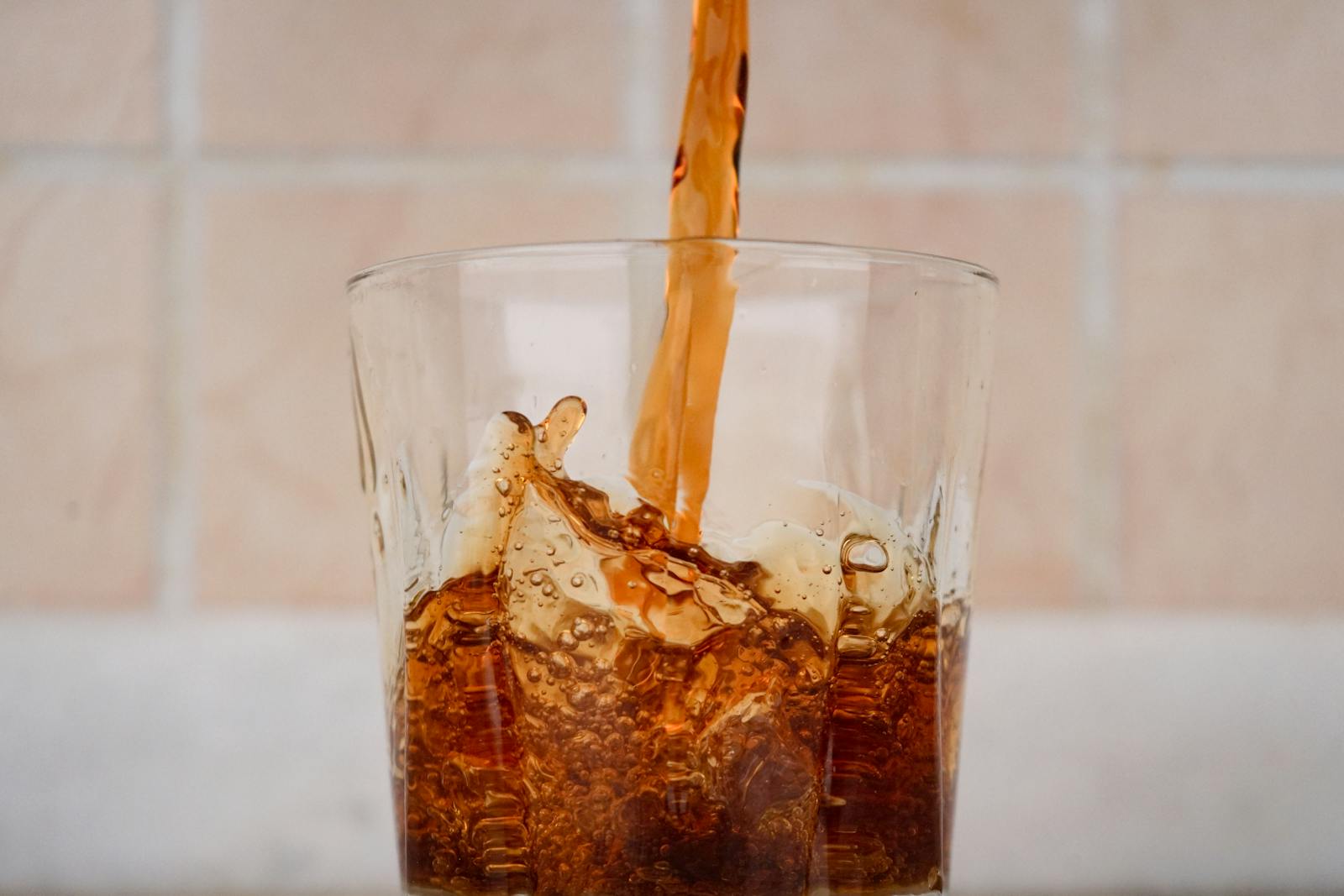 Close-up view of cola being poured into a glass with a splash effect, showcasing refreshing texture.