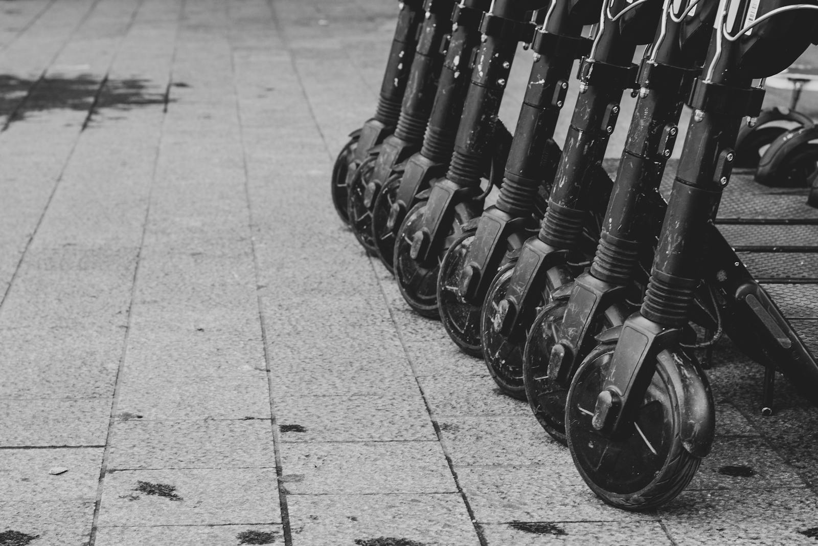 Black and white photo of lined-up electric scooters on pavement in Brussels.