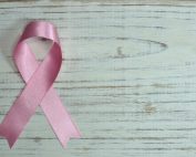A pink ribbon symbolizing cancer awareness placed on a light wooden background.