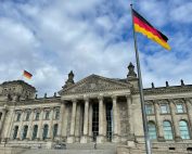 The iconic Reichstag building in Berlin with a German flag against a blue sky, symbolizing democracy.