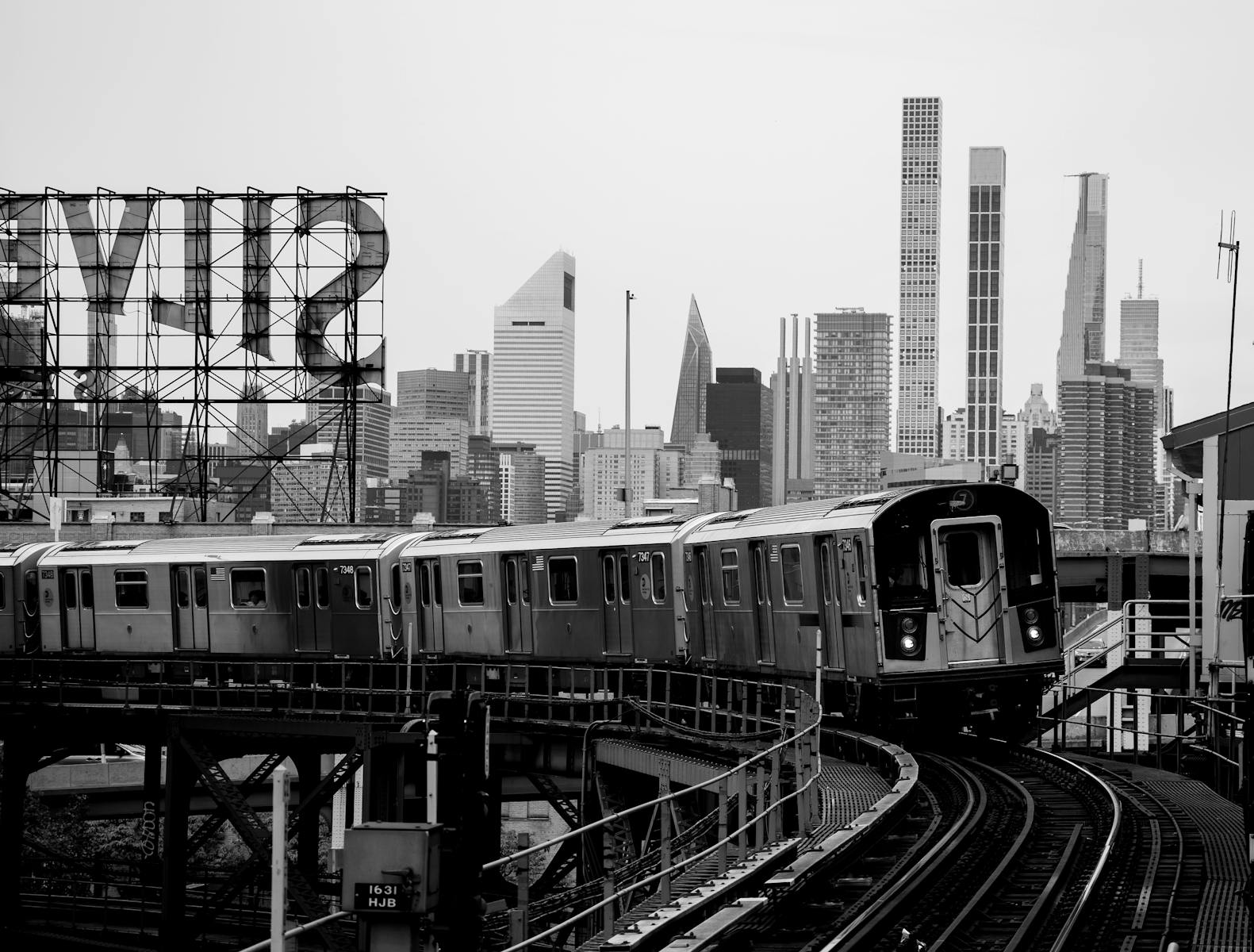 Black and white image of an elevated train and New York City skyline with recognizable landmarks.