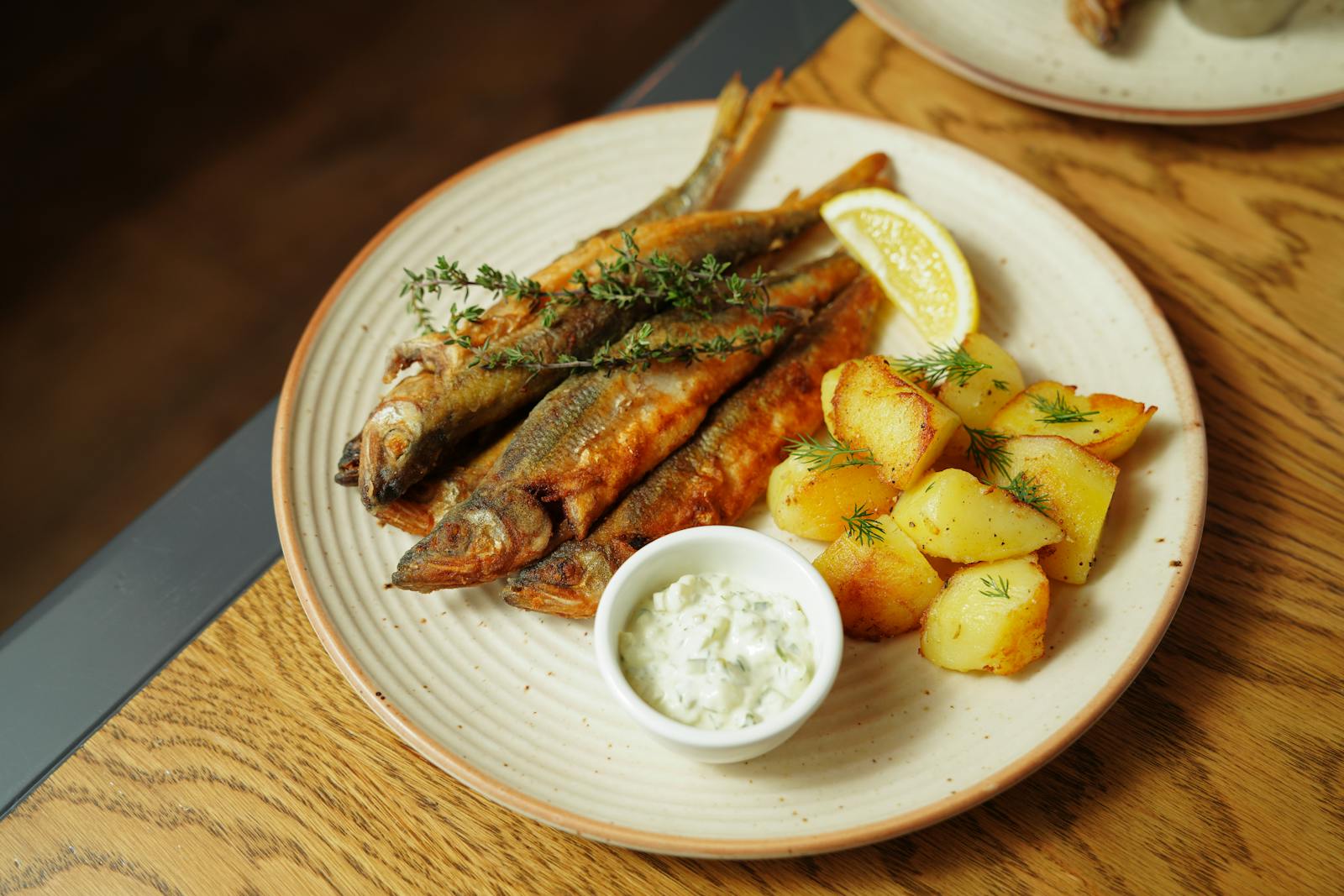 Plate of crispy fish with lemon, roasted potatoes, and creamy dip.