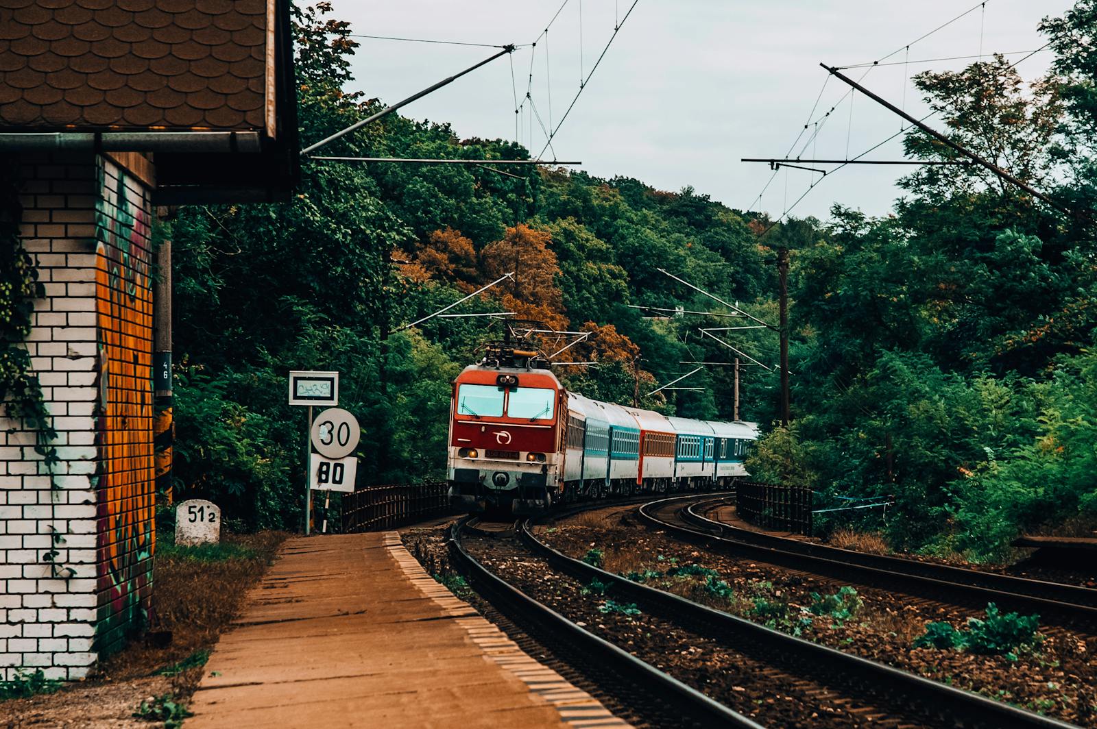 A train moves along railway tracks amidst a vibrant forest landscape near Bratislava, Slovakia.