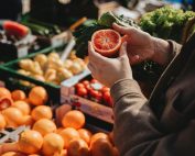 A close-up of a person holding a sliced orange at an outdoor market, showcasing fresh produce.