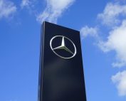 Elegant Mercedes Benz logo on a tall sign with a bright blue sky background.