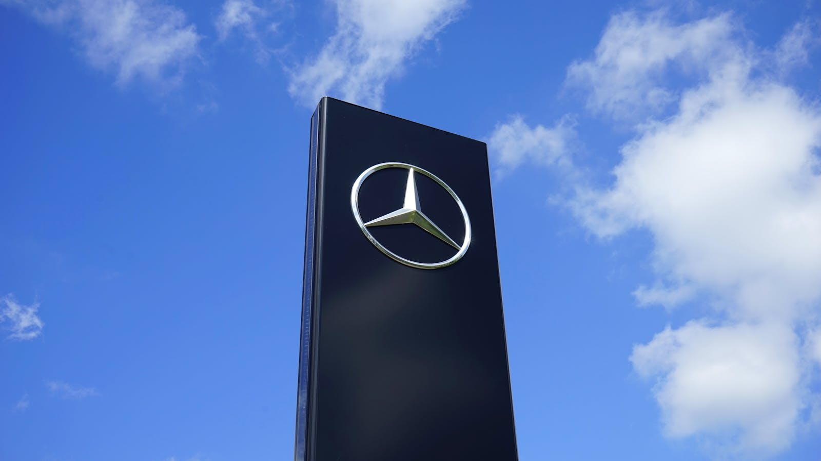 Elegant Mercedes Benz logo on a tall sign with a bright blue sky background.