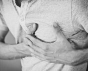 Black and white photo of a man clutching his chest, indicating discomfort or pain.
