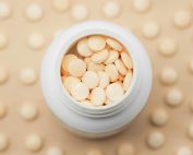 High-angle shot of a white bottle filled with round tablets on a textured background.