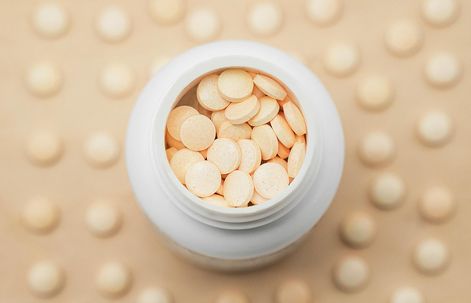 High-angle shot of a white bottle filled with round tablets on a textured background.