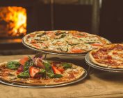 Trio of gourmet pizzas with unique toppings near a wood-fired oven, ideal for food enthusiasts.
