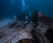 Two scuba divers exploring a shipwreck in the deep ocean waters of Isla Mujeres, Mexico.