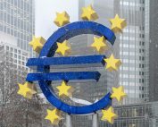 The iconic Euro symbol stands prominently amidst snowy Frankfurt skyscrapers.