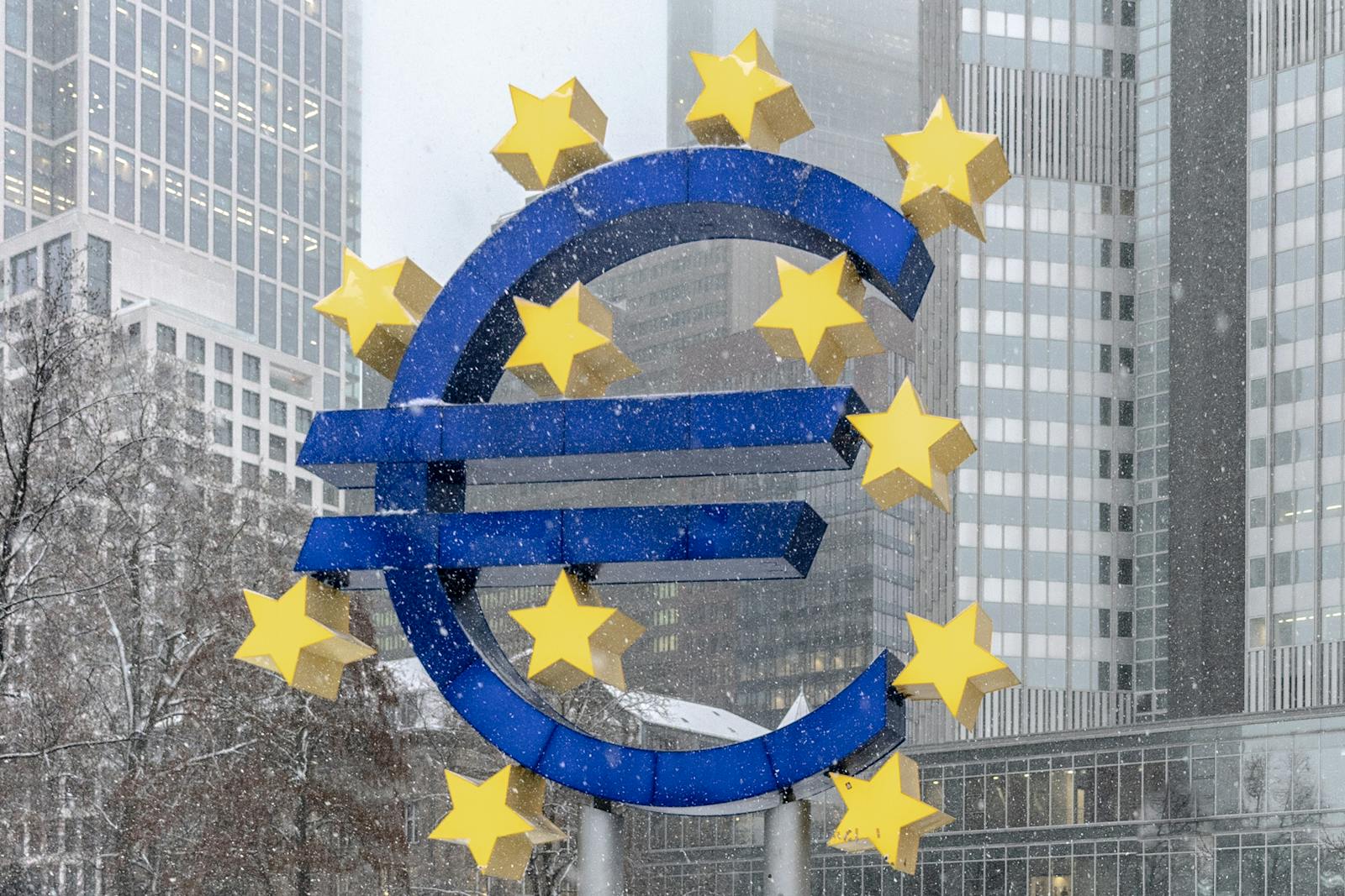 The iconic Euro symbol stands prominently amidst snowy Frankfurt skyscrapers.