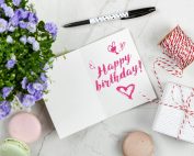 Charming birthday greeting card layout with macarons, flowers, and gift box.