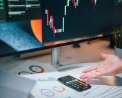 Businessman analyzing stock market data on computer monitor with documents and calculator.