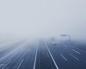 A fog-covered highway with vehicles disappearing into the mist, creating a mysterious and tranquil scene.