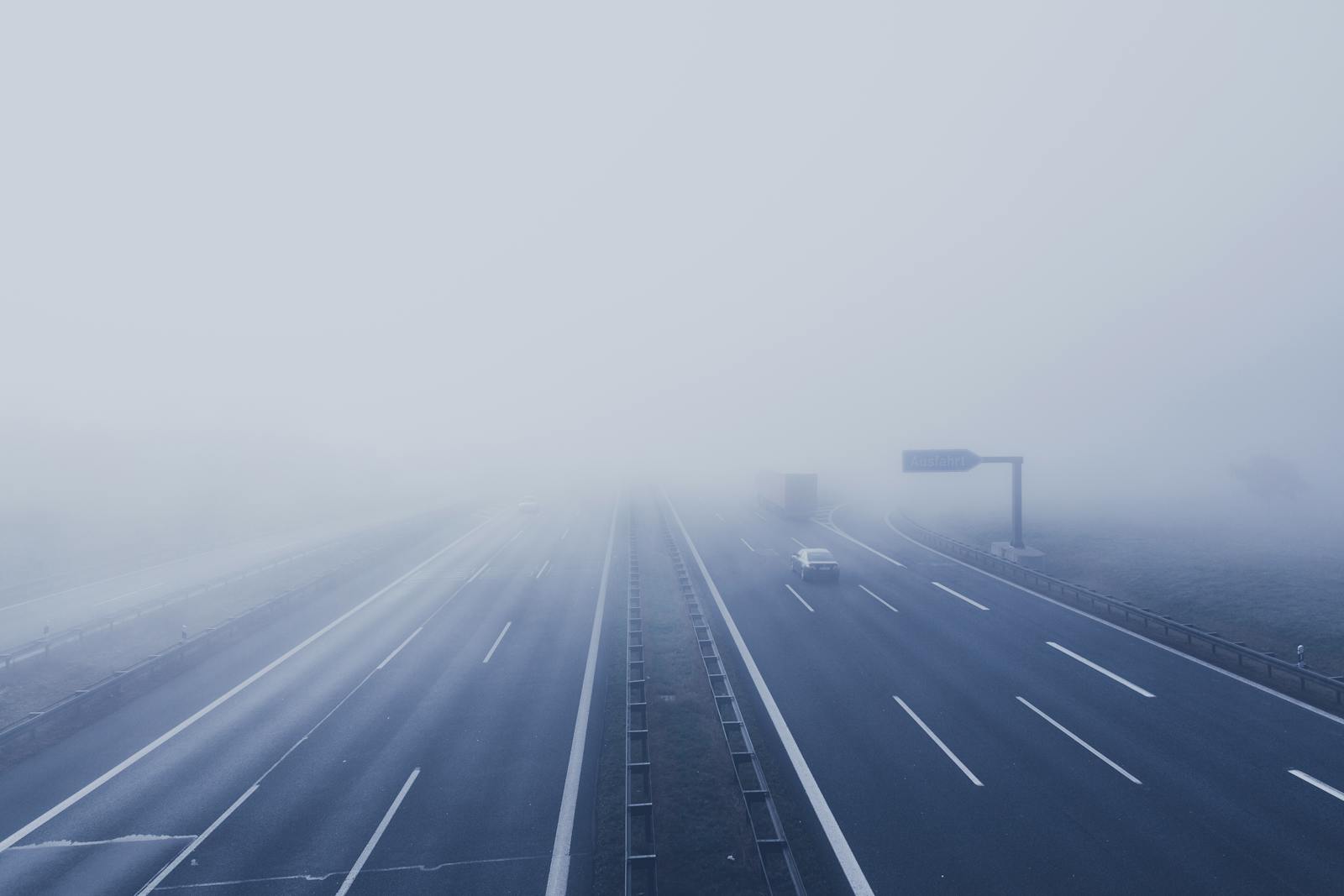 A fog-covered highway with vehicles disappearing into the mist, creating a mysterious and tranquil scene.