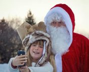 A young girl takes a selfie with Santa Claus in a snowy outdoors setting.