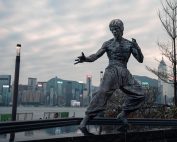Statue of Bruce Lee in martial arts pose with Hong Kong skyline backdrop.