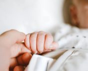 Close-up of a newborn's hand gently gripping a parent's finger, symbolizing love and connection.
